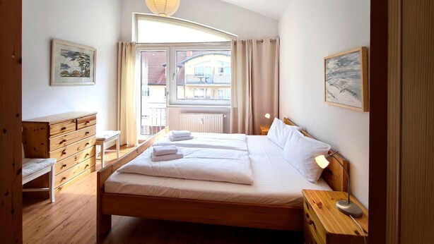A bedroom with a bed, bedside tables, a dresser, a window with curtains, and artwork on the walls.