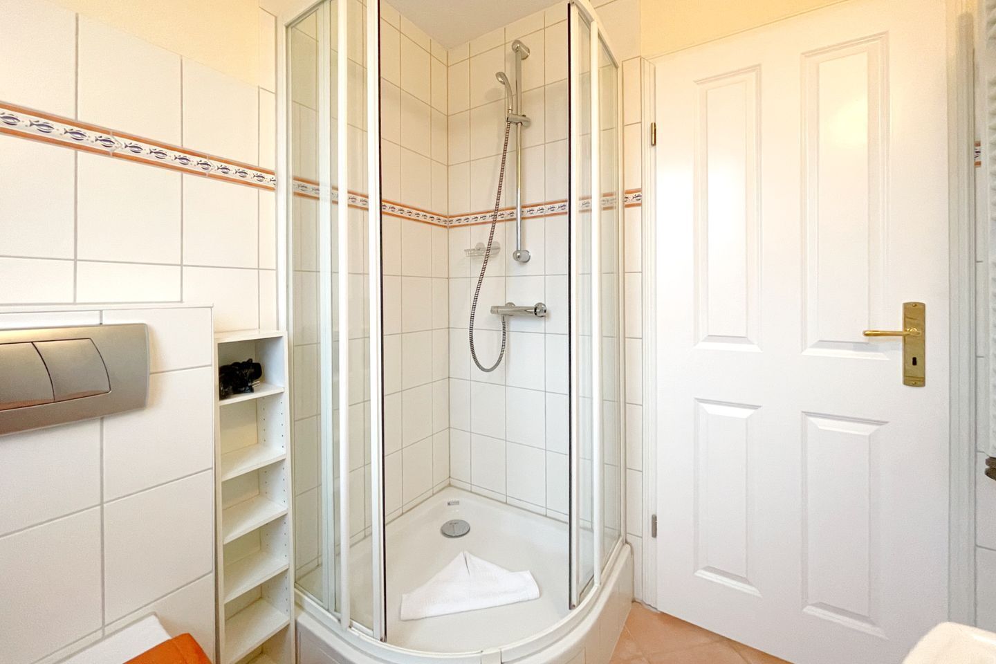 A modern bathroom with a glass-enclosed shower, white tiled walls, and a door with a gold handle.