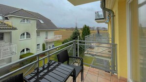 A balcony with a table and chairs, overlooking a residential area with houses and a clear sky.