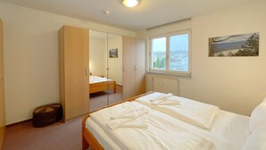 A bedroom with a bed, a window with a view, a radiator, and a door leading to another room.