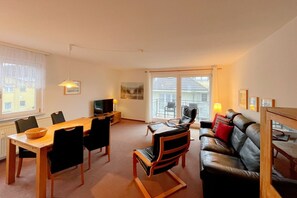 A modern living room with a dining area, a sofa, a TV, and a balcony with a view. - "Relaxation and comfort: Your vacation apartment on Usedom awaits you!" - (Loddin)