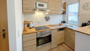 A compact kitchen with wooden cabinets, a microwave, a stove, and a dishwasher.