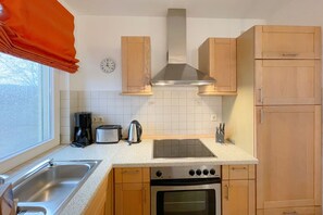 Eine kleine Küche mit Holzausstattung, einem Edelstahl-Spülbecken, einem Herd, einem Toaster und einem Wasserkocher.