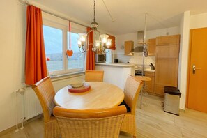Eine kompakte Küche mit Essbereich, ausgestattet mit einem runden Holztisch, Korbstühlen und einer Pendelleuchte.