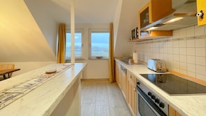 A modern kitchen with a marble countertop, wooden cabinets, a built-in oven, and a window providing a view of the outdoors.