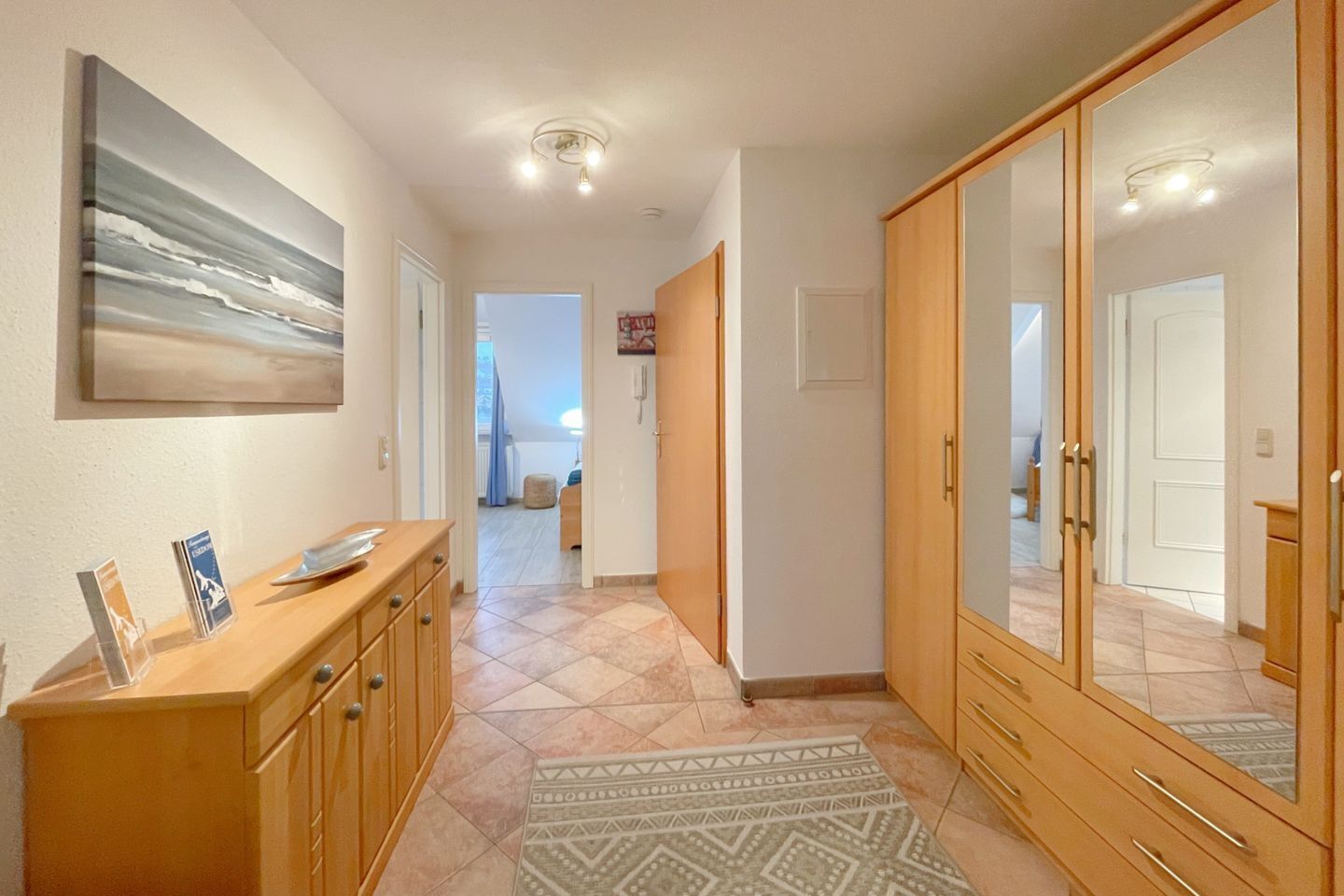 A hallway with a wooden cabinet, a patterned rug, and a large mirror.