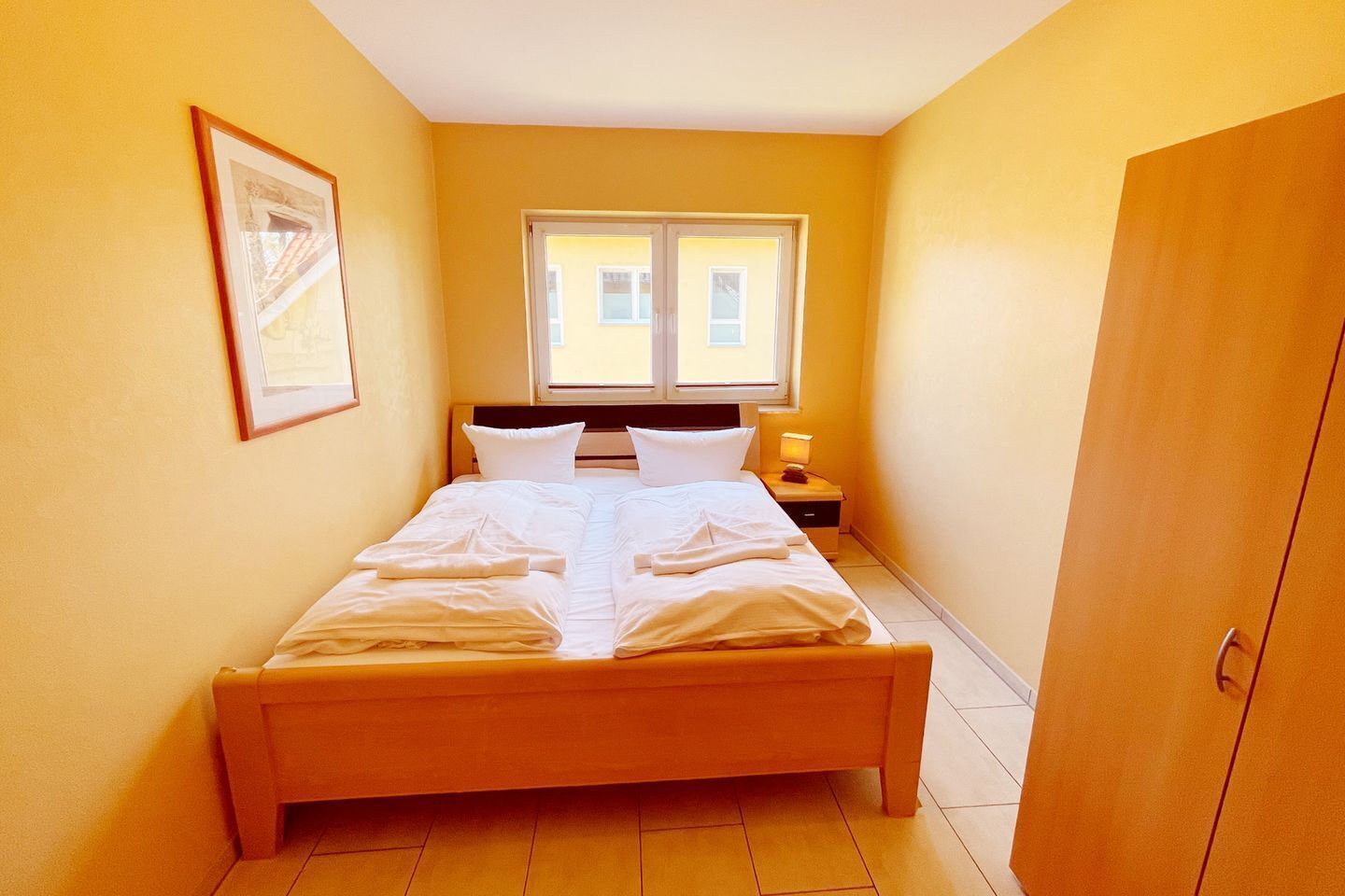 Una habitación pequeña y luminosa con una cama individual, una mesita de noche, una ventana y una puerta.