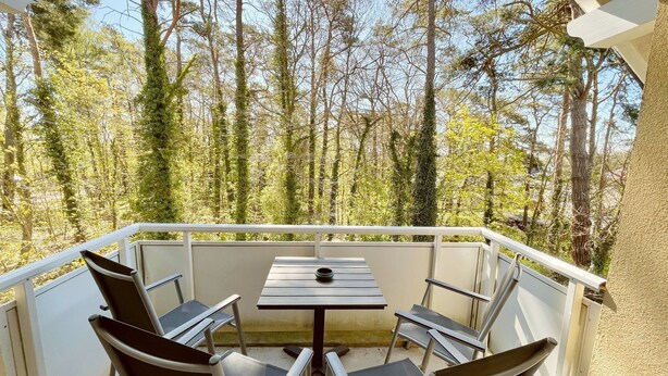 A balcony with a table and chairs, surrounded by trees.