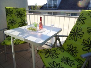 Un petit balcon avec une table dressée pour deux personnes, agrémentée d’une bouteille de vin et d’un verre.