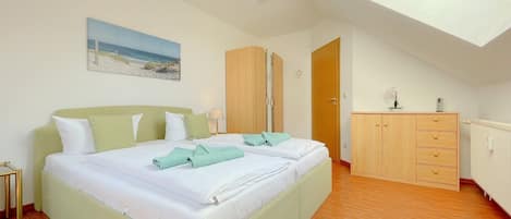 A bedroom with a bed, a wooden wardrobe, a painting, and a skylight.
