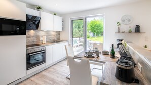 Une cuisine moderne avec des meubles blancs, un four encastré et un coin repas comprenant une table et des chaises.
