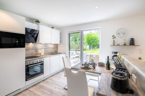 A modern kitchen with white cabinetry, a built-in oven, and a dining area with a table and chairs. - Hochwertig, Liebevoll Eingerichtetes, 48qm Großes, Ferienhaus für 3 Personen. - Gerhart-hauptmann (Loddin)
