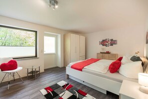 A modern bedroom with a bed, a chair, a desk, and a window with a view of trees. - Hochwertig, Liebevoll Eingerichtetes, 85qm Großes, Ferienhaus für 4 Personen. - Gerhart-hauptmann (Loddin)
