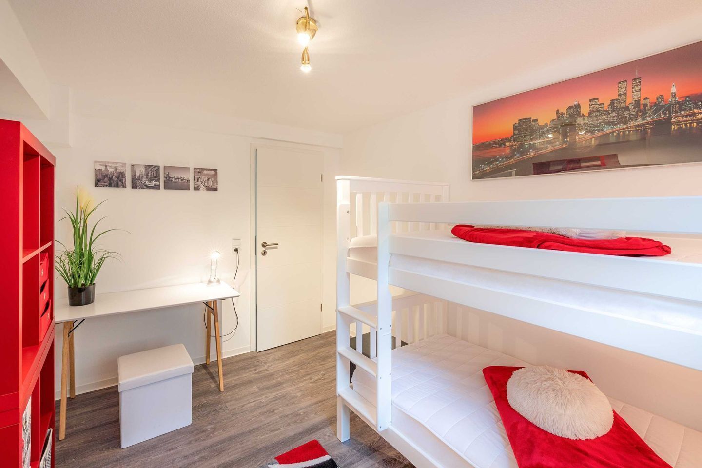 A room with bunk beds, a desk, and a cityscape painting.