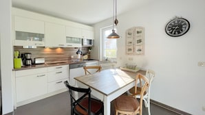 Et moderne køkken med hvide skabe, en træbordplade, et spisebord med stole, en hængende lampe og et vægur.
