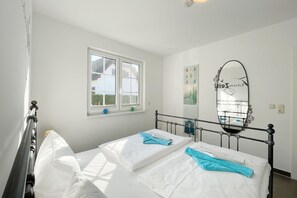 Een slaapkamer met een bed, een raam, een spiegel aan de muur en een klein prentje.