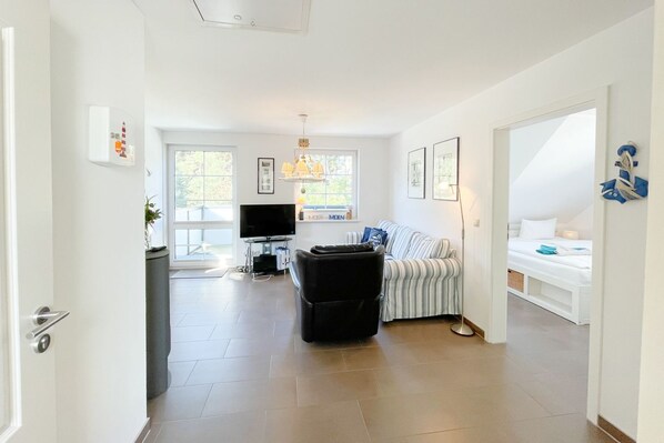 A modern living room with a sofa, a TV, and a dining area with a table and chairs.
