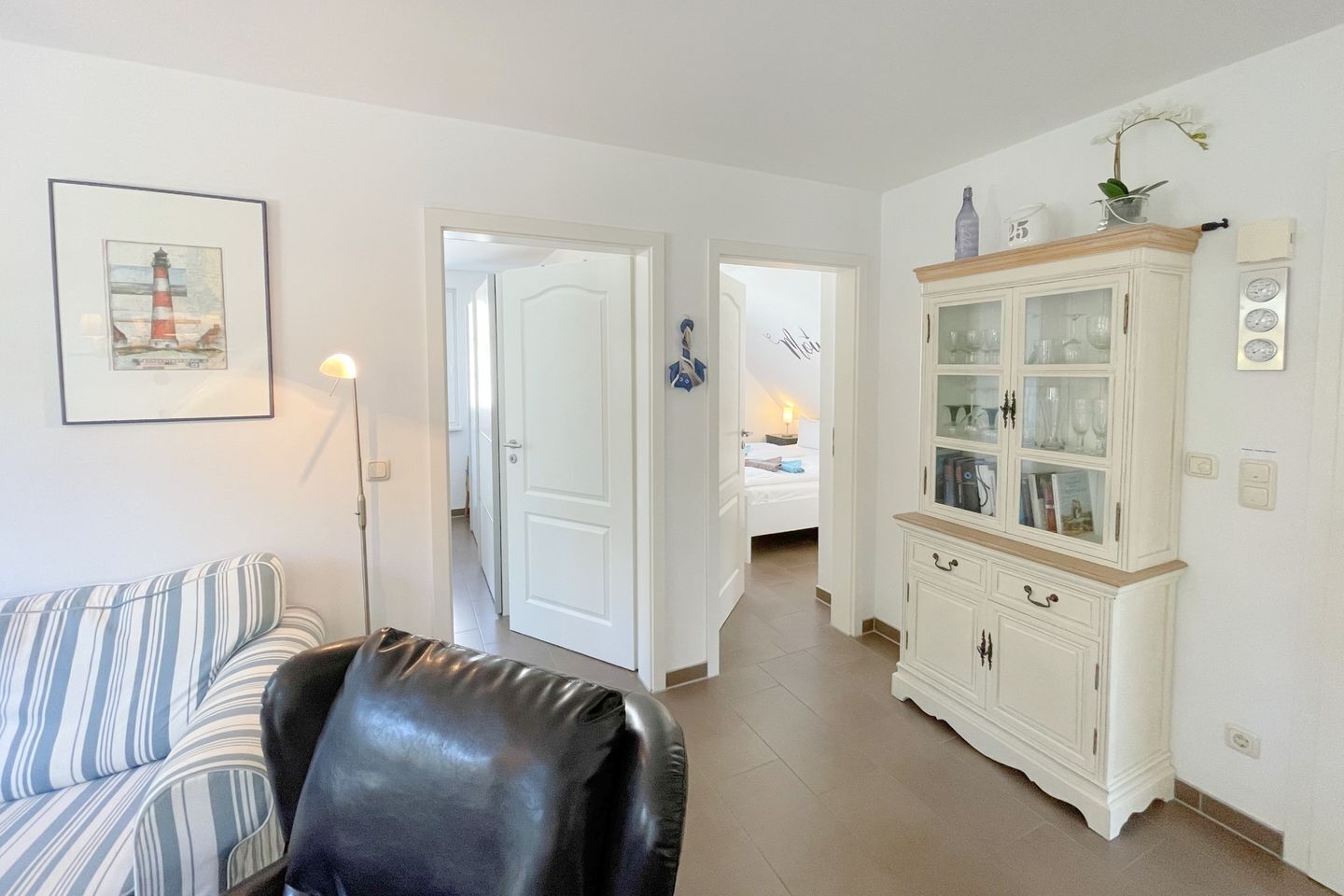 Una sala de estar con un sofá a rayas, un sillón de cuero, un aparador blanco con puertas de vidrio y un cuadro en la pared.