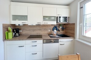 A compact kitchen with white cabinets, a microwave, a coffee maker, and a sink.