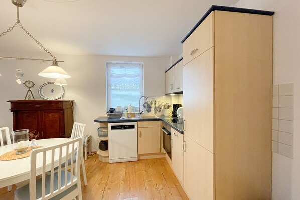 A compact kitchen with a dishwasher, a window, and a dining area with a white table and chairs.