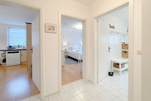 A modern interior with a kitchen, a bedroom with a bed and nightstand, and a bathroom with a shower and storage shelves.