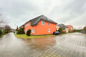 Een woonstraat met huizen, een geparkeerde auto en een nat voetpad.