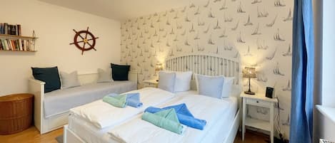 Une chambre avec deux lits, une bibliothèque, un gouvernail de bateau fixé au mur et un papier peint à motifs.