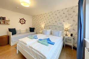 A bedroom with two beds, a bookshelf, a wall-mounted ship's wheel, and a patterned wallpaper.