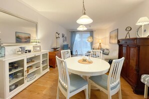 A dining area with a round table, white chairs, a wooden cabinet, and a mirror on the wall.