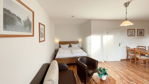 A bedroom with a bed, a sofa, a dining table with chairs, and a ceiling fan. - "Relax in the charming vacation apartment on the Usedom coast!" - (Loddin)