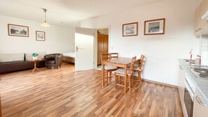 A modern apartment with a wooden floor, a dining area with wooden chairs, a kitchen with a stove, and a living area with a sofa and a coffee table. - "Relax in the charming vacation apartment on the Usedom coast!" - (Loddin)