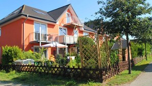 A two-story house with a balcony, a wooden fence, and a garden. - "Relax in the charming vacation apartment on the Usedom coast!" - (Loddin)