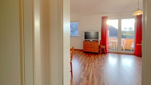 A room with a wooden floor, a television on a wooden cabinet, and a sliding glass door leading to an outdoor area with a table and chairs. - "Relax in the charming vacation apartment on the Usedom coast!" - (Loddin)