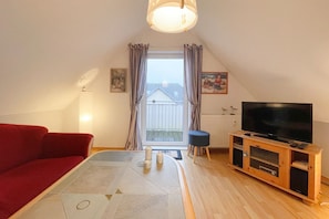 Una sala de estar acogedora con un sofá rojo, un mueble de televisión de madera y un ventanal con cortinas.