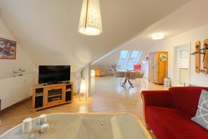 Un amplio loft con techos altos, un televisor sobre un mueble de madera, una zona de comedor con mesa y sillas, y un sofá rojo.