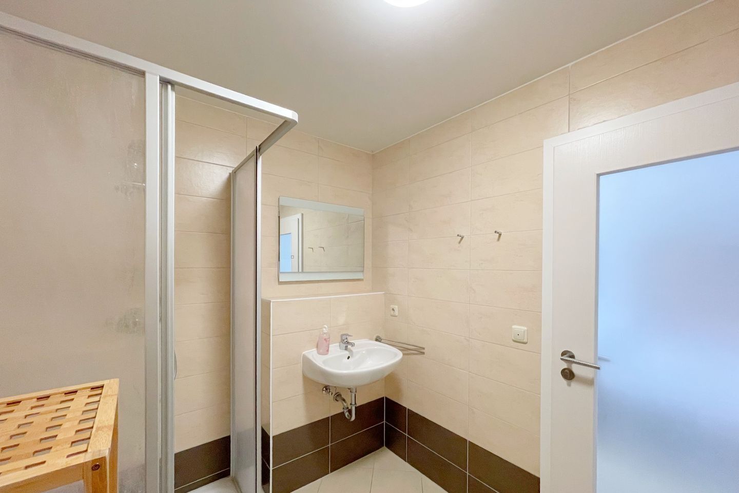 A bathroom with a shower, sink, mirror, and a door.