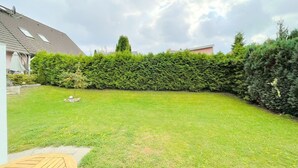 A backyard with a well-maintained lawn, a wooden deck, and a tall hedge. - "Experience unforgettable days in the "Engel" vacation bungalow on the Baltic Sea!" - To (Ückeritz)