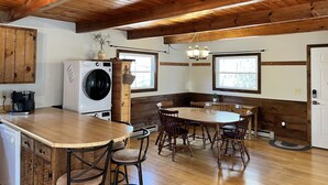 Une cuisine équipée d’un lave-linge et d’un sèche-linge intégrés, de meubles en bois, d’une grande table à manger avec des chaises et d’un plafond en bois.
