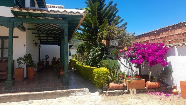 A courtyard with potted plants, a pergola, and a white building with a tiled roof. - Hotel Casa san rafael  (Villa de Leyva)