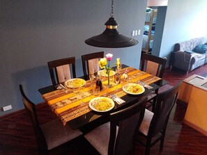 Mesa de comedor preparada para cuatro personas, con mantel estampado, platos de comida y una lámpara colgante.