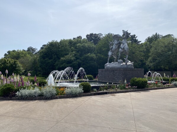 A large outdoor fountain with water jets, surrounded by a garden with various plants and flowers.