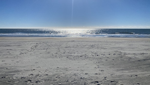 Une plage avec des empreintes de pas dans le sable et un ciel dégagé.