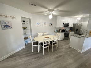 A modern kitchen with white cabinets, a dining area with a round table and chairs, a ceiling fan, and a microwave.