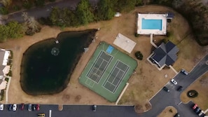 An aerial view of a property with a swimming pool, tennis court, and a pond.