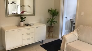 A bedroom with a white bed, a white dresser with drawers, a mirror above the dresser, a potted plant, and a black rug. - Large one bedroom Cottage in the heart of St Marys (Saint Marys)