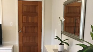 A hallway with a wooden door, a white console table, a potted orchid, and a mirror on the wall. - Large one bedroom Cottage in the heart of St Marys (Saint Marys)