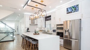 A modern kitchen with a large island, stainless steel appliances, and a glass railing overlooking a cityscape. - Gatsby`s Corner | King Bed | Near Parks & Golf (Surrey)