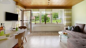 Ein Wohnzimmer mit Essbereich, einer Couch, einem Fernseher und Blick auf Grünflächen.