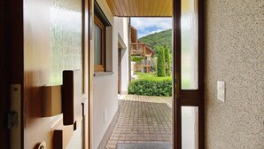 Ein Durchgang zu einem gepflasterten Außenbereich mit einem Holzbalkon und Blick auf Berge.