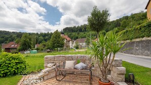 Eine Steinsitzbank mit Kissen, ein Topfpflanze und ein Weg, der zu einem Haus mit rotem Dach führt.